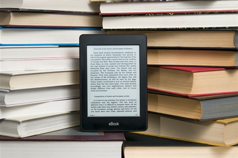 An eReader propped among a pile of books