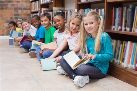 Multicultural children sitting in front of a bookshelf, looking at the camera